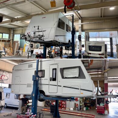 A white motorhome is raised on a hydraulic lift inside a workshop, with tools and equipment scattered nearby.